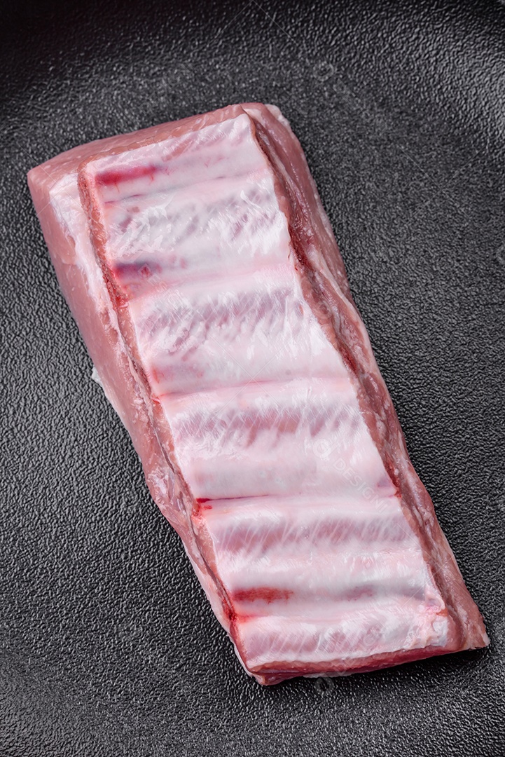 Costelas de porco cruas com sal, especiarias e ervas em fundo de concreto texturizado