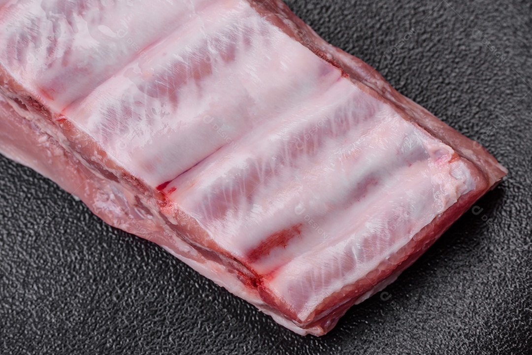 Costelas de porco cruas com sal, especiarias e ervas em fundo de concreto texturizado