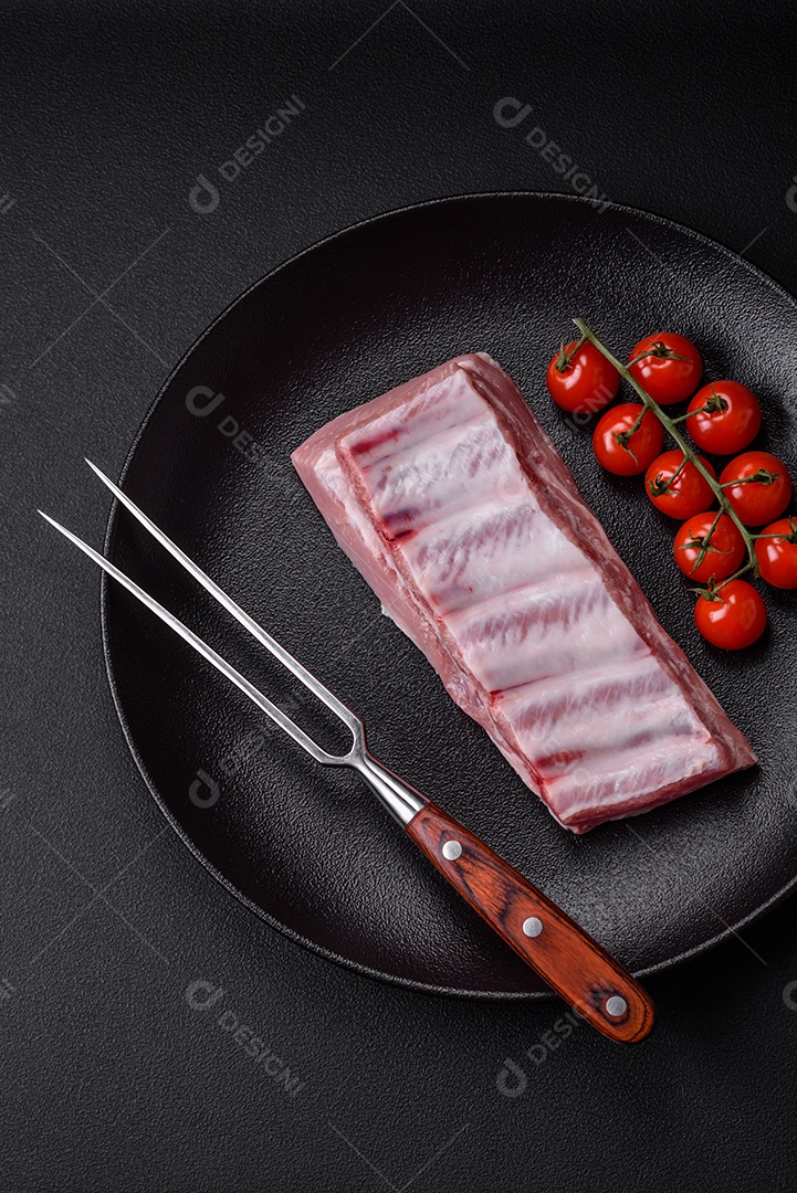 Costelas de porco cruas com sal, especiarias e ervas em fundo de concreto texturizado