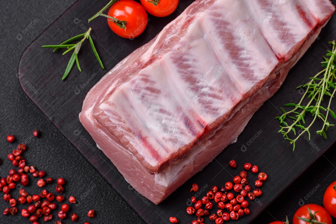 Costelas de porco cruas com sal, especiarias e ervas em fundo de concreto texturizado