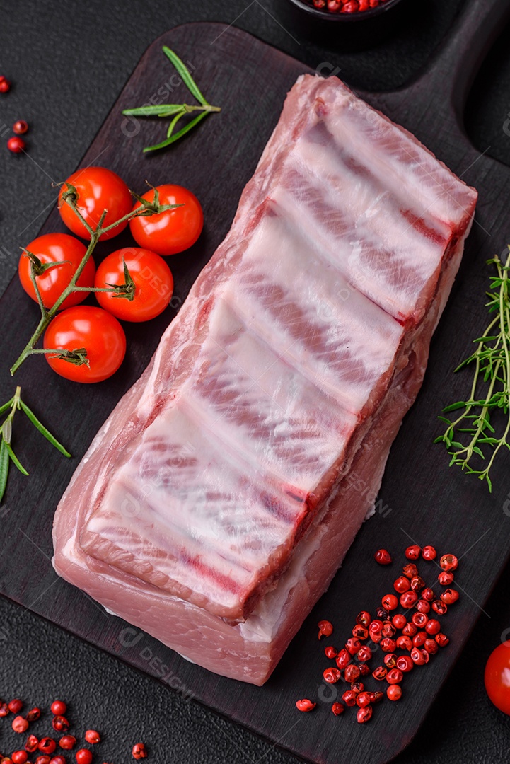 Costelas de porco cruas com sal, especiarias e ervas em fundo de concreto texturizado