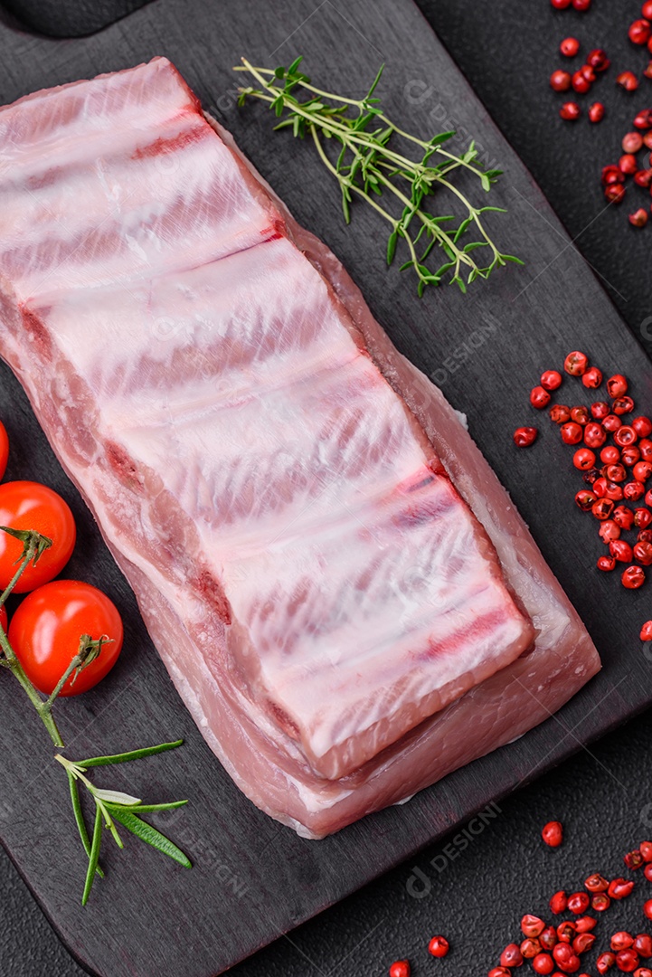 Costelas de porco cruas com sal, especiarias e ervas em fundo de concreto texturizado