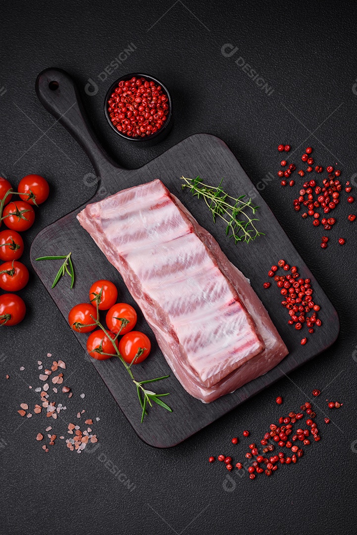 Costelas de porco cruas com sal, especiarias e ervas em fundo de concreto texturizado