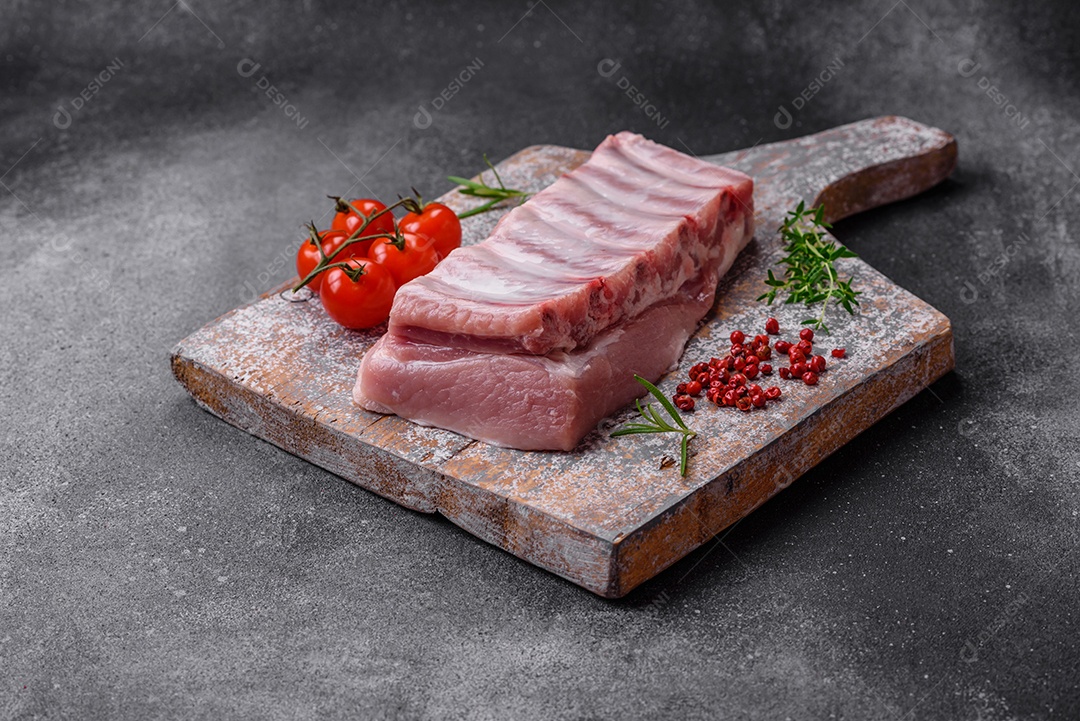 Costelas de porco cruas com sal, especiarias e ervas em fundo de concreto texturizado