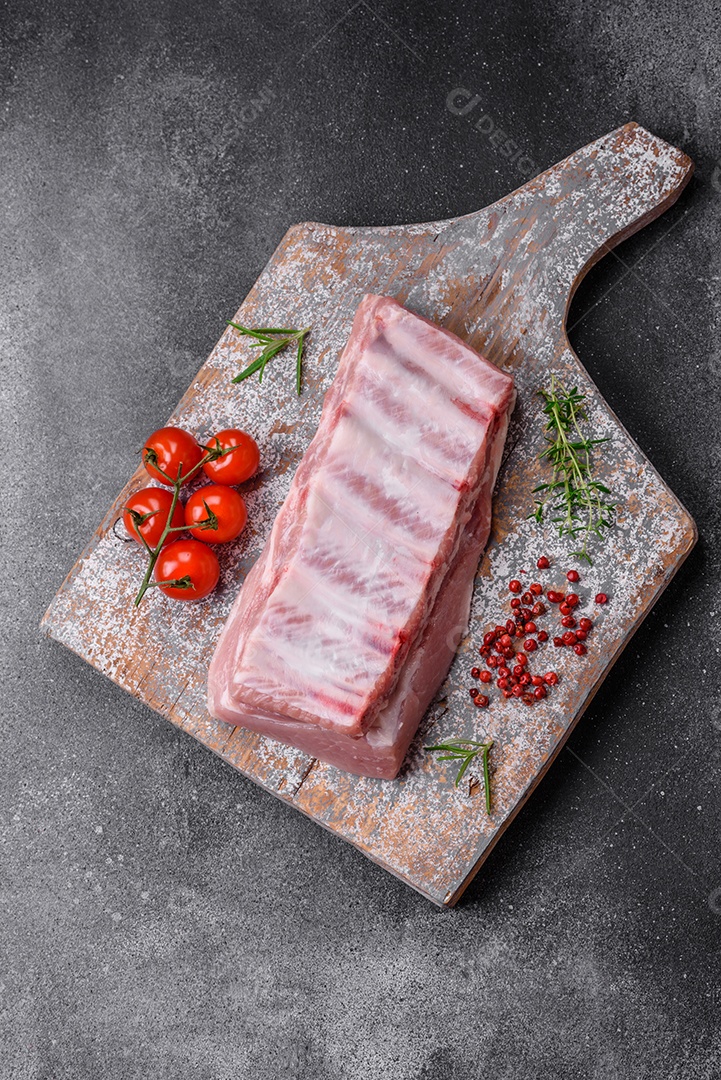 Costelas de porco cruas com sal, especiarias e ervas em fundo de concreto texturizado