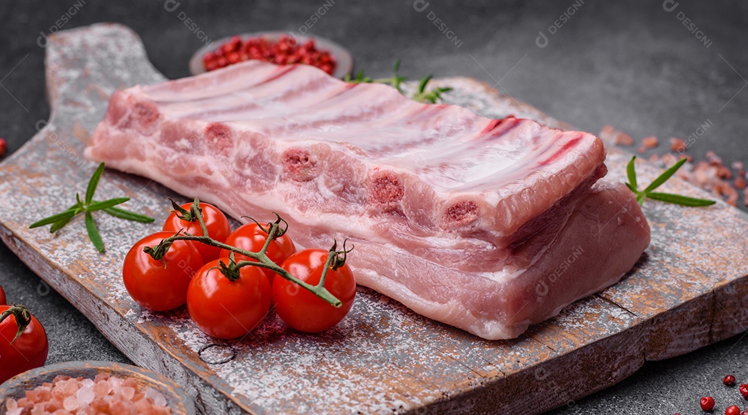 Costelas de porco cruas com sal, especiarias e ervas em fundo de concreto texturizado