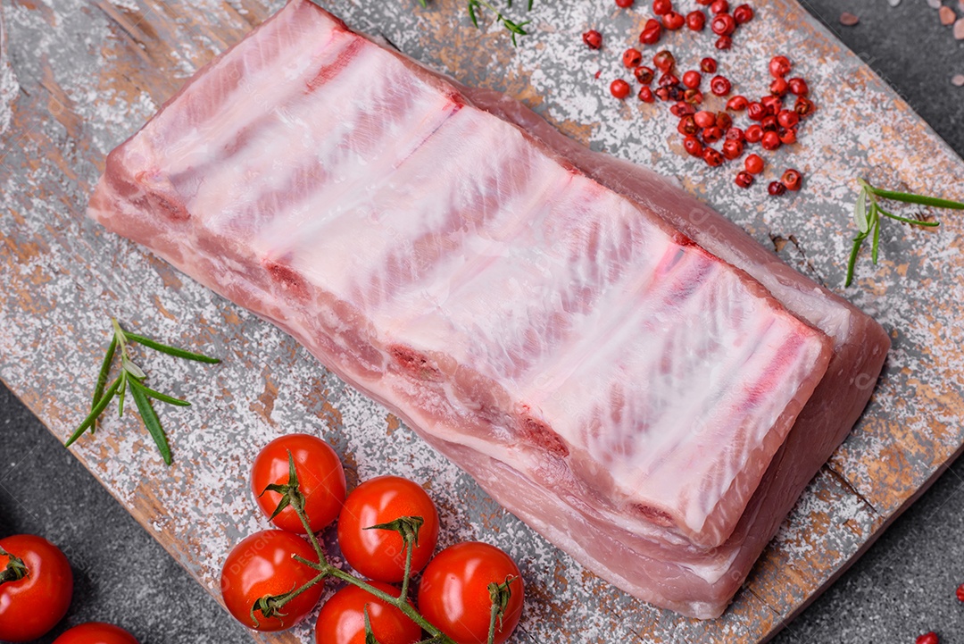 Costelas de porco cruas com sal, especiarias e ervas em fundo de concreto texturizado