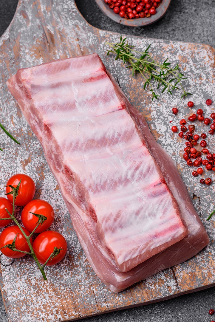 Costelas de porco cruas com sal, especiarias e ervas em fundo de concreto texturizado