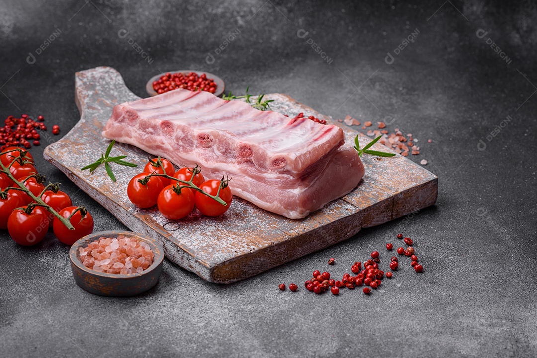 Costelas de porco cruas com sal, especiarias e ervas em fundo de concreto texturizado