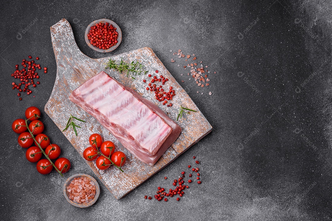 Costelas de porco cruas com sal, especiarias e ervas em fundo de concreto texturizado