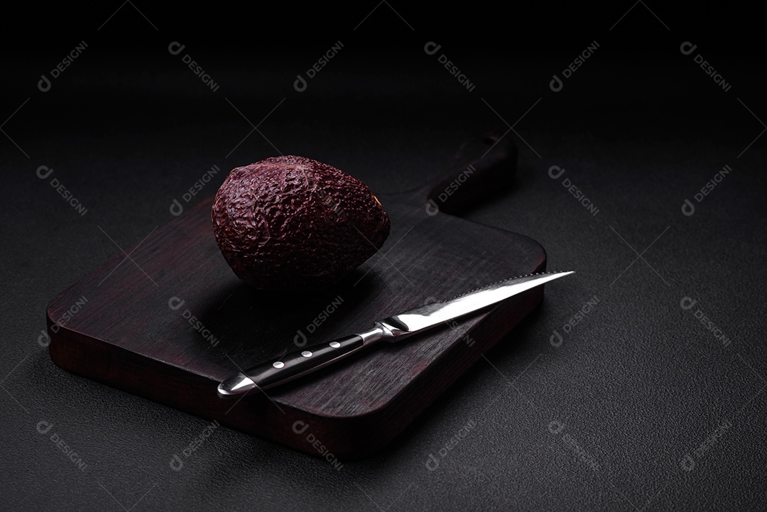 Abacate fresco, maduro e de cor marrom suave sobre um fundo escuro de concreto. Ingredientes culinários saudáveis