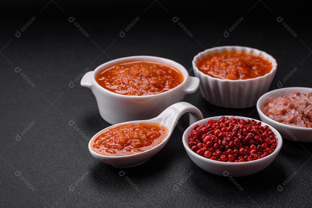 Delicioso molho de tomate picante com pimenta, alho, sal, especiarias e ervas em uma molheira branca sobre um fundo escuro de concreto