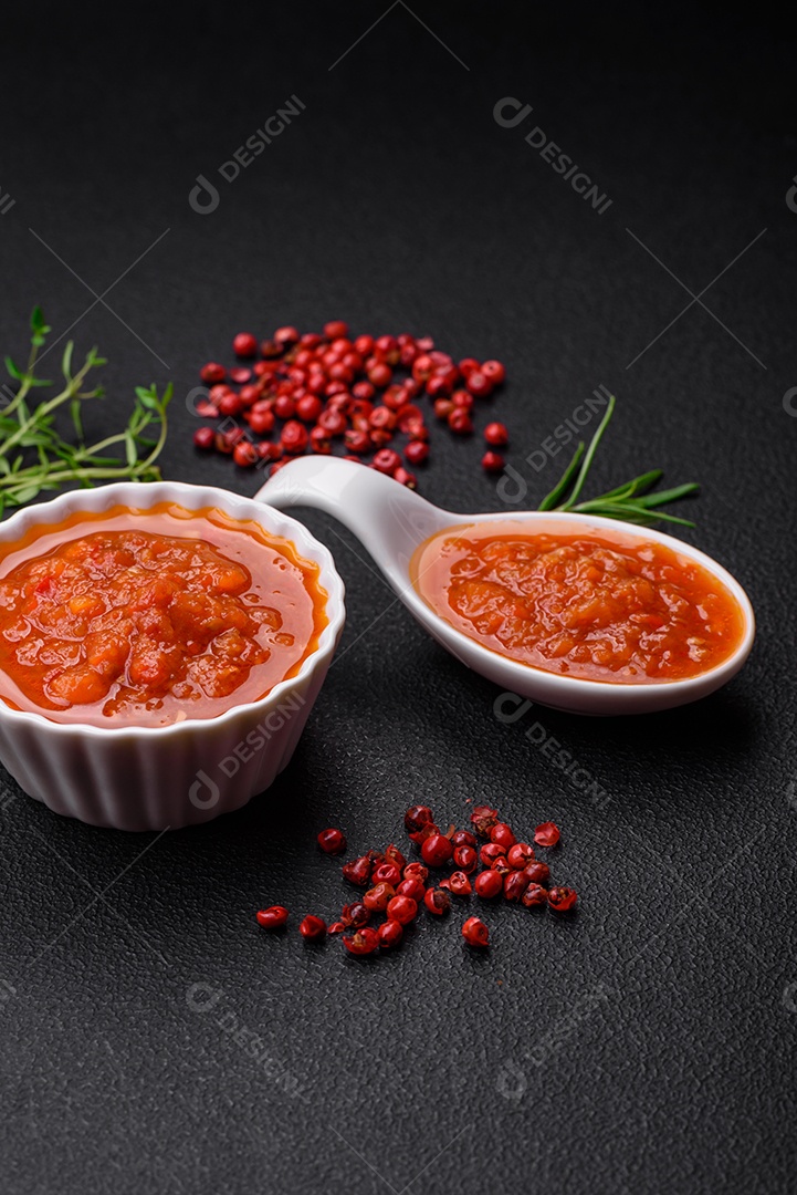 Delicioso molho de tomate picante com pimenta, alho, sal, especiarias e ervas em uma molheira branca sobre um fundo escuro de concreto