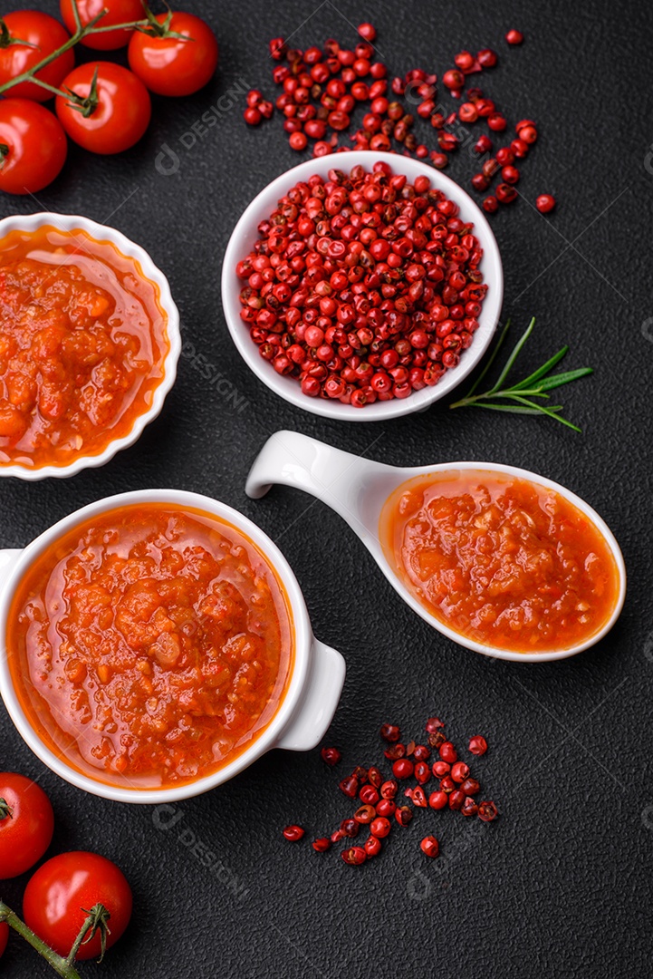 Delicioso molho de tomate picante com pimenta, alho, sal, especiarias e ervas em uma molheira branca sobre um fundo escuro de concreto