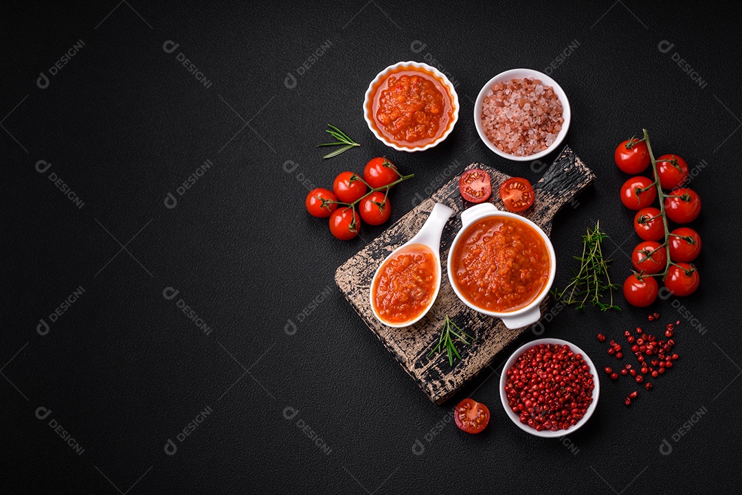 Delicioso molho de tomate picante com pimenta, alho, sal, especiarias e ervas em uma molheira branca sobre um fundo escuro de concreto