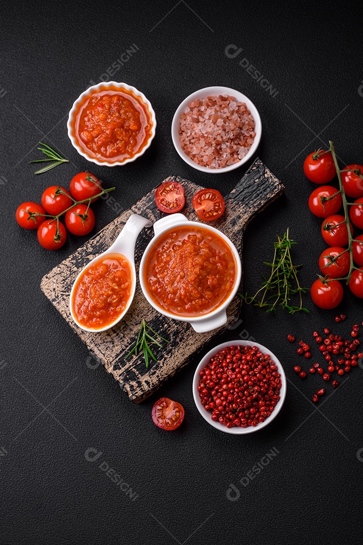 Delicioso molho de tomate picante com pimenta, alho, sal, especiarias e ervas em uma molheira branca sobre um fundo escuro de concreto