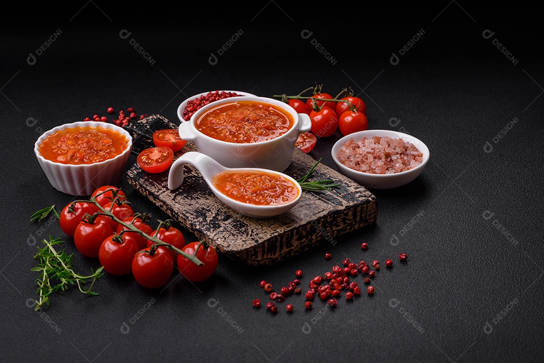 Delicioso molho de tomate picante com pimenta, alho, sal, especiarias e ervas em uma molheira branca sobre um fundo escuro de concreto