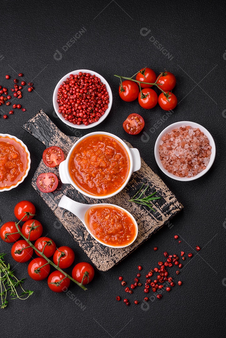 Delicioso molho de tomate picante com pimenta, alho, sal, especiarias e ervas em uma molheira branca sobre um fundo escuro de concreto