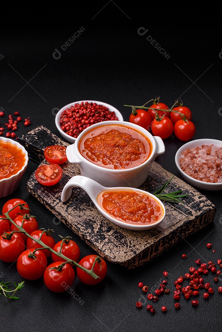 Delicioso molho de tomate picante com pimenta, alho, sal, especiarias e ervas em uma molheira branca sobre um fundo escuro de concreto