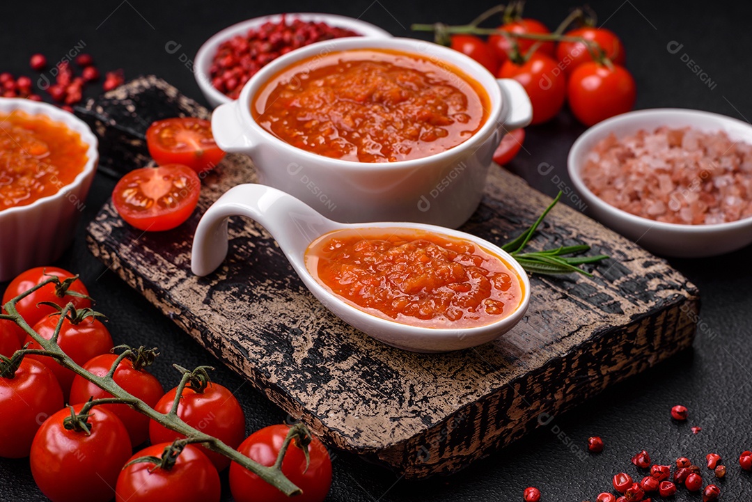 Delicioso molho de tomate picante com pimenta, alho, sal, especiarias e ervas em uma molheira branca sobre um fundo escuro de concreto