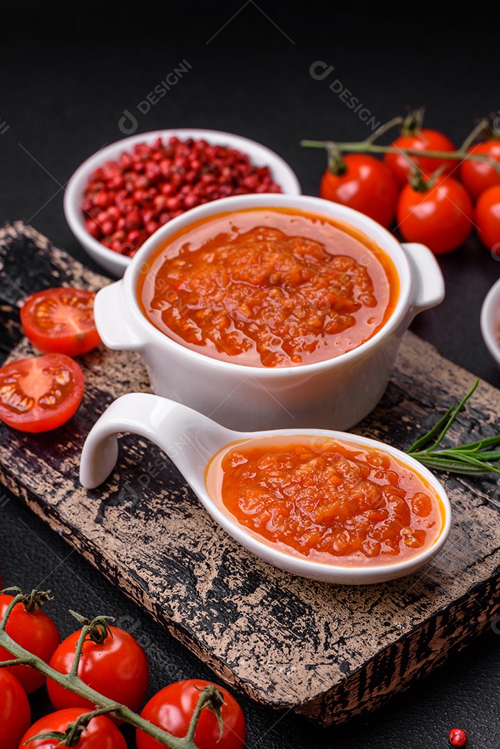 Delicioso molho de tomate picante com pimenta, alho, sal, especiarias e ervas em uma molheira branca sobre um fundo escuro de concreto