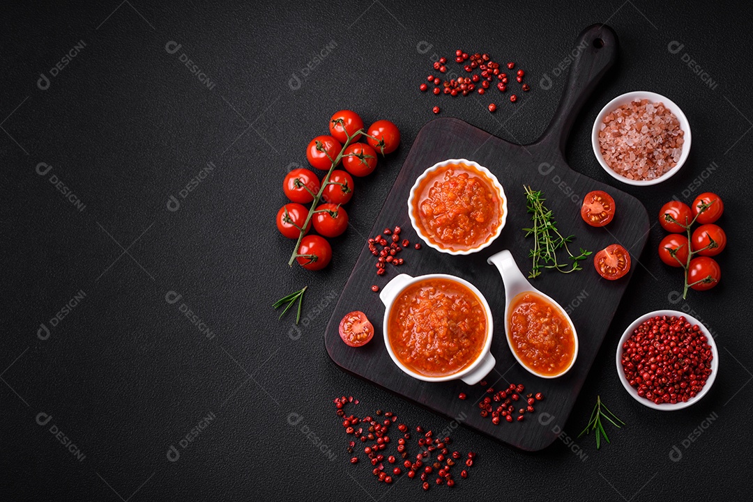 Delicioso molho de tomate picante com pimenta, alho, sal, especiarias e ervas em uma molheira branca sobre um fundo escuro de concreto
