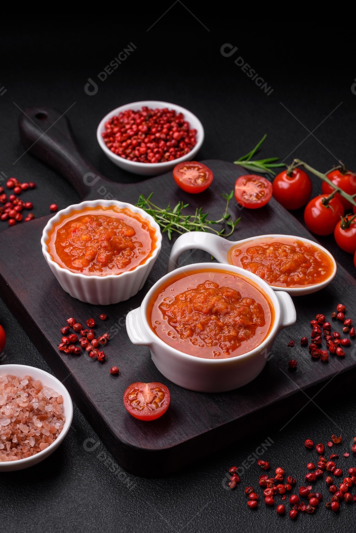 Delicioso molho de tomate picante com pimenta, alho, sal, especiarias e ervas em uma molheira branca sobre um fundo escuro de concreto
