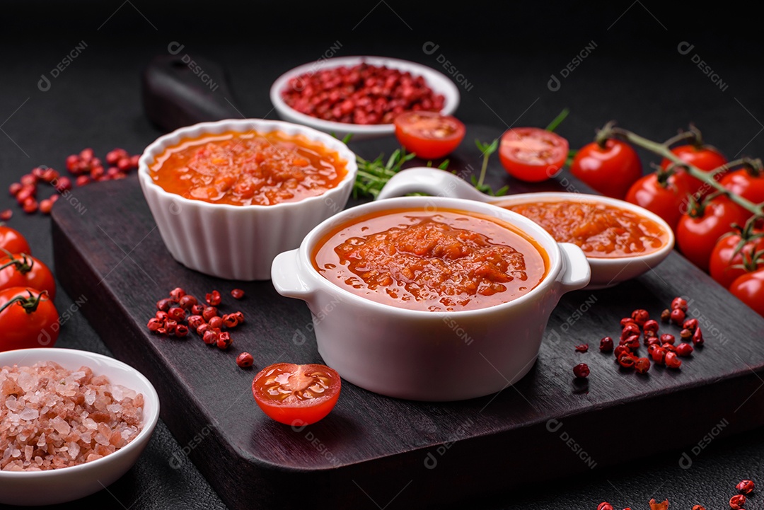 Delicioso molho de tomate picante com pimenta, alho, sal, especiarias e ervas em uma molheira branca sobre um fundo escuro de concreto