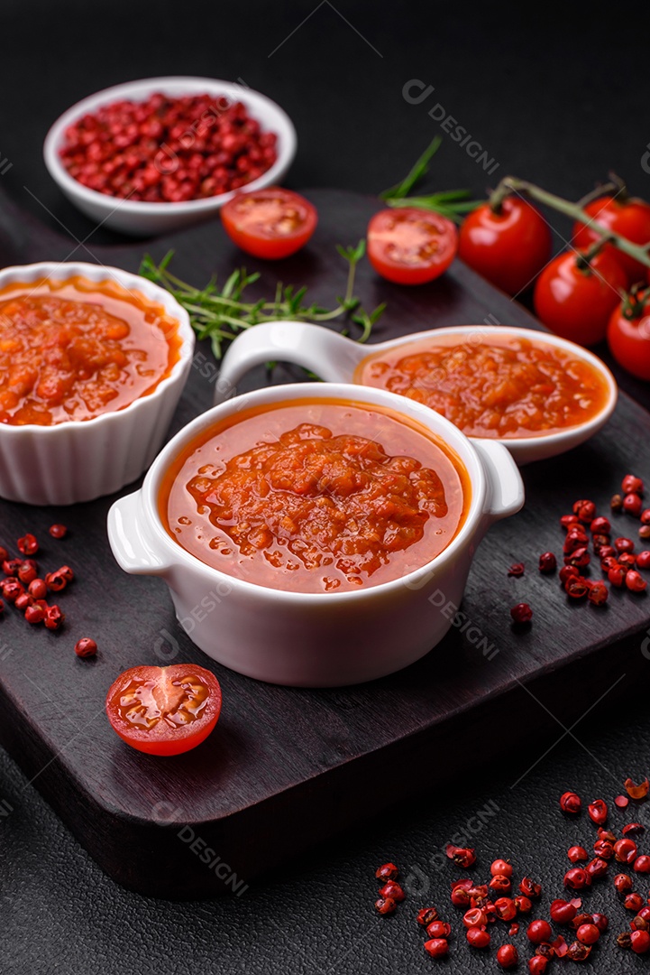 Delicioso molho de tomate picante com pimenta, alho, sal, especiarias e ervas em uma molheira branca sobre um fundo escuro de concreto