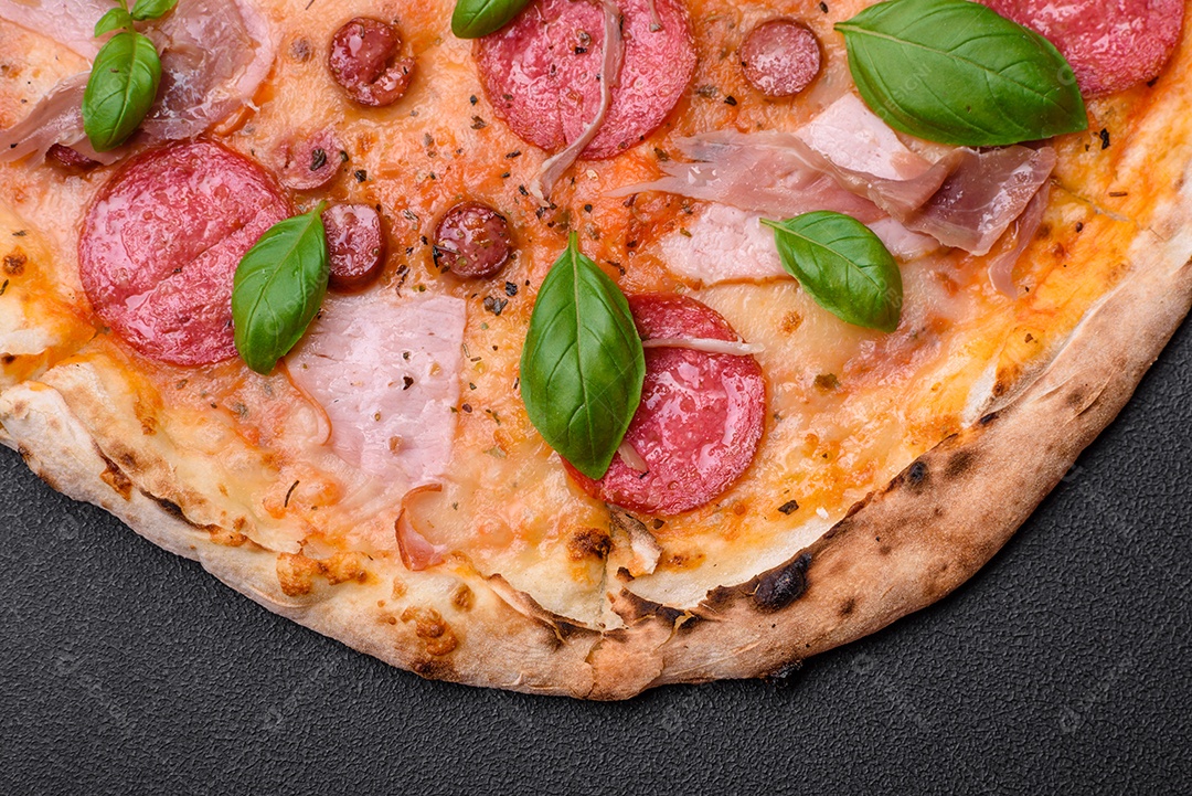Deliciosa pizza assada em forno fresco com salame, carne, queijo, tomate, especiarias e ervas sobre um fundo escuro de concreto