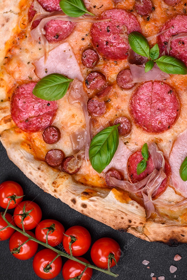 Deliciosa pizza assada em forno fresco com salame, carne, queijo, tomate, especiarias e ervas sobre um fundo escuro de concreto