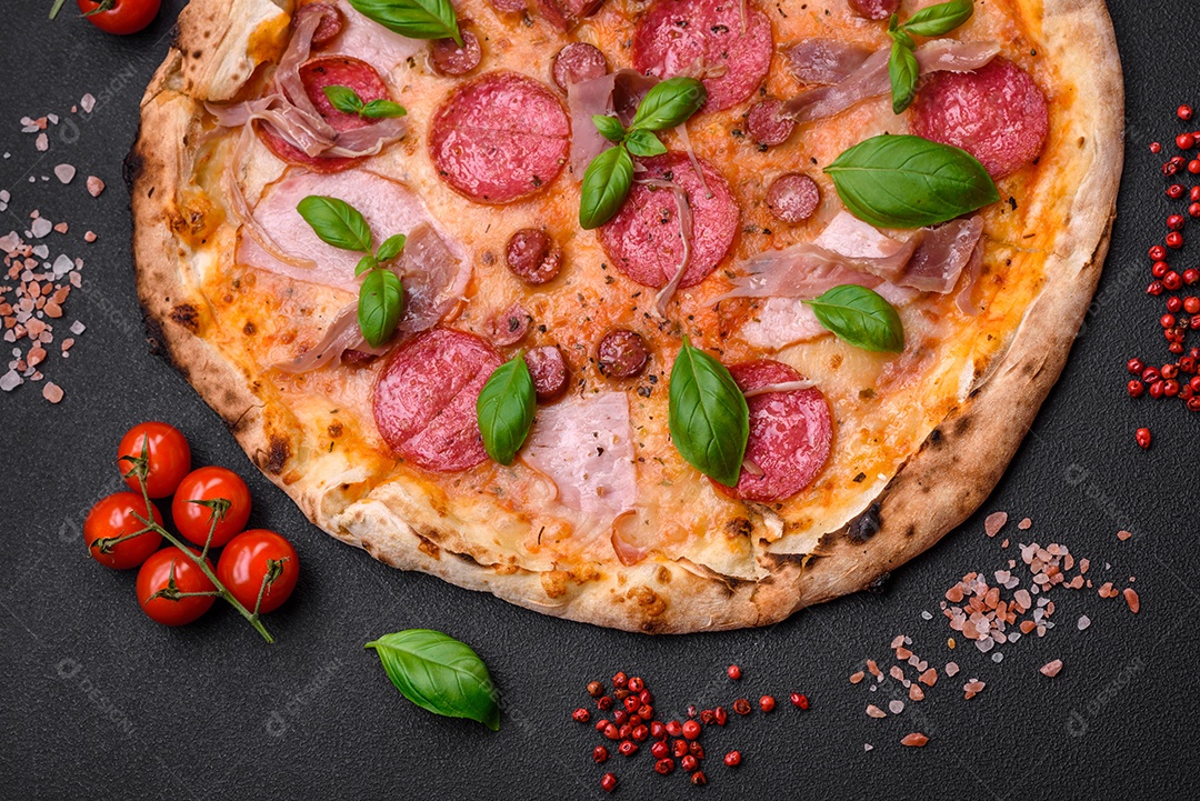 Deliciosa pizza assada em forno fresco com salame, carne, queijo, tomate, especiarias e ervas sobre um fundo escuro de concreto