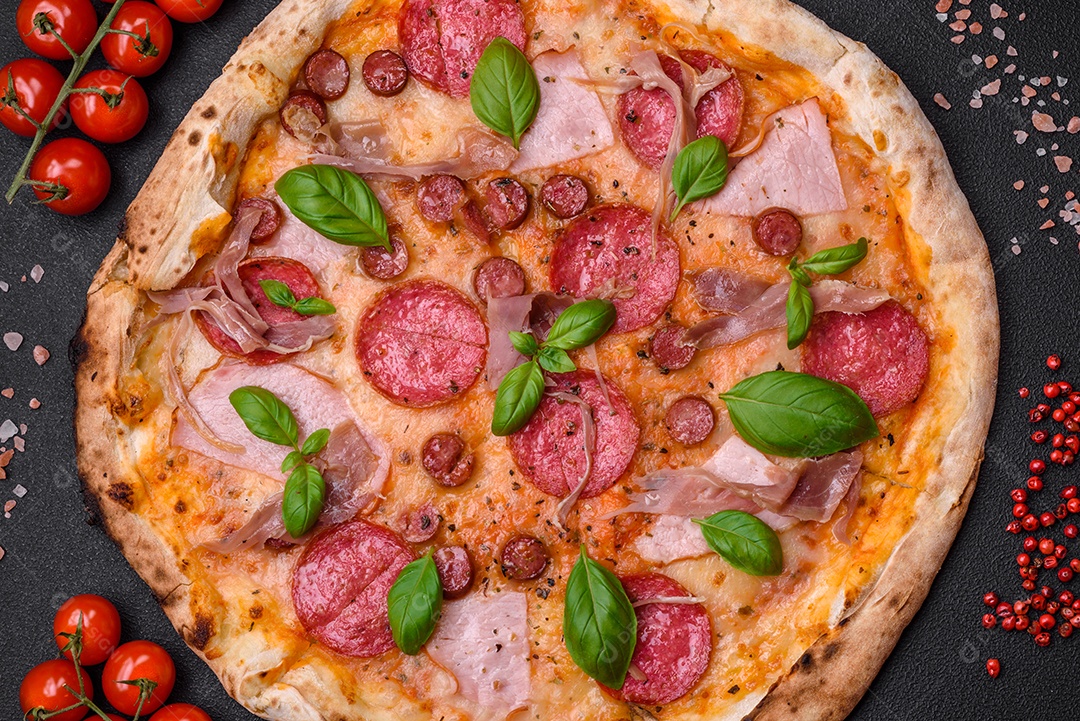 Deliciosa pizza assada em forno fresco com salame, carne, queijo, tomate, especiarias e ervas sobre um fundo escuro de concreto