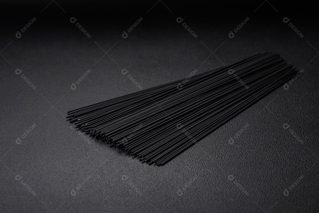 Massa de espaguete preta crua com tomate, sal, especiarias e ervas sobre um fundo escuro de concreto