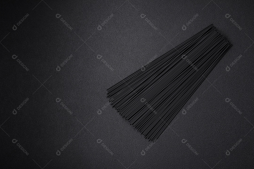 Massa de espaguete preta crua com tomate, sal, especiarias e ervas sobre um fundo escuro de concreto