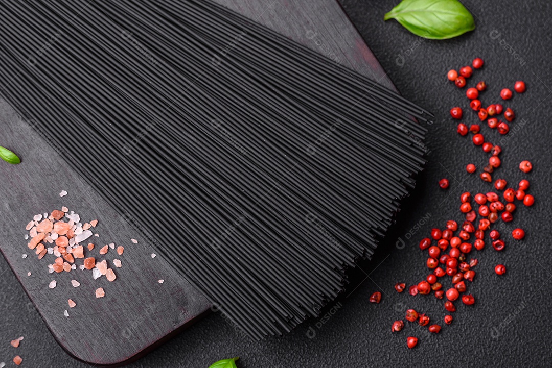 Massa de espaguete preta crua com tomate, sal, especiarias e ervas sobre um fundo escuro de concreto