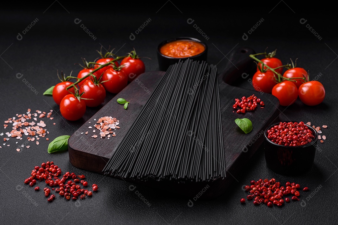 Massa de espaguete preta crua com tomate, sal, especiarias e ervas sobre um fundo escuro de concreto