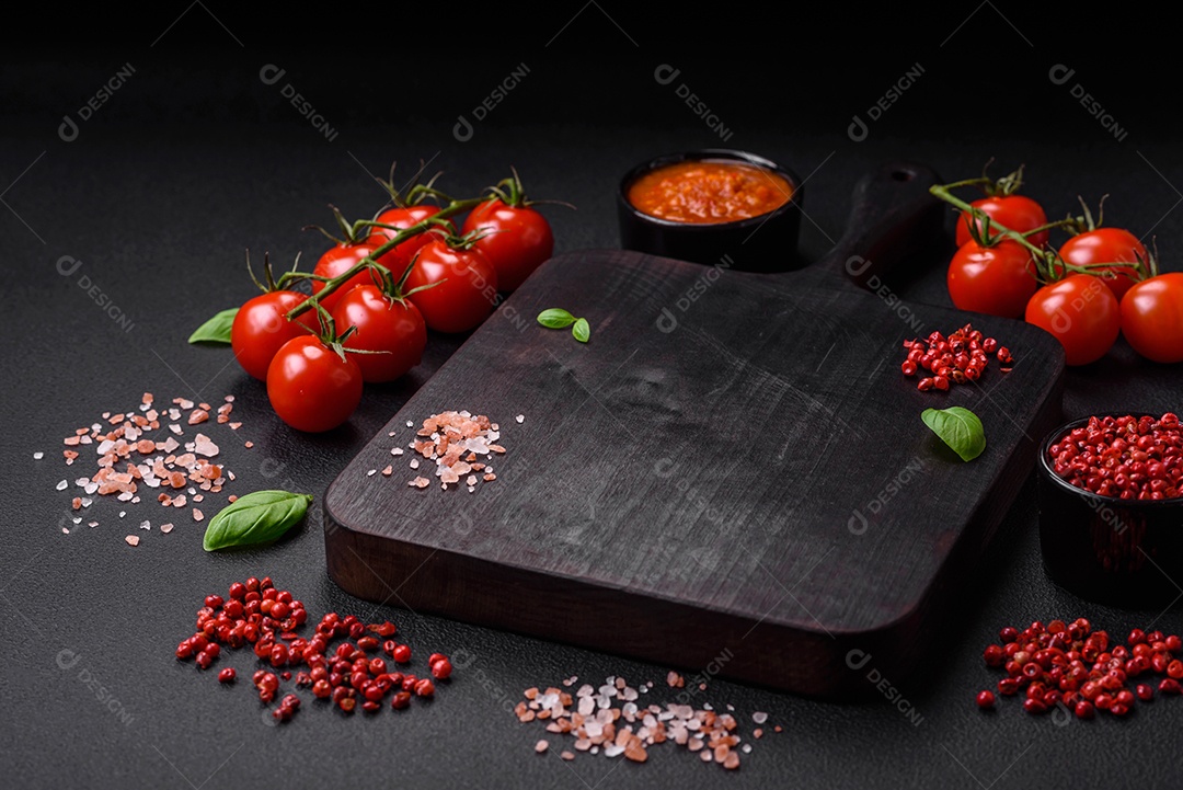 Massa de espaguete preta crua com tomate, sal, especiarias e ervas sobre um fundo escuro de concreto