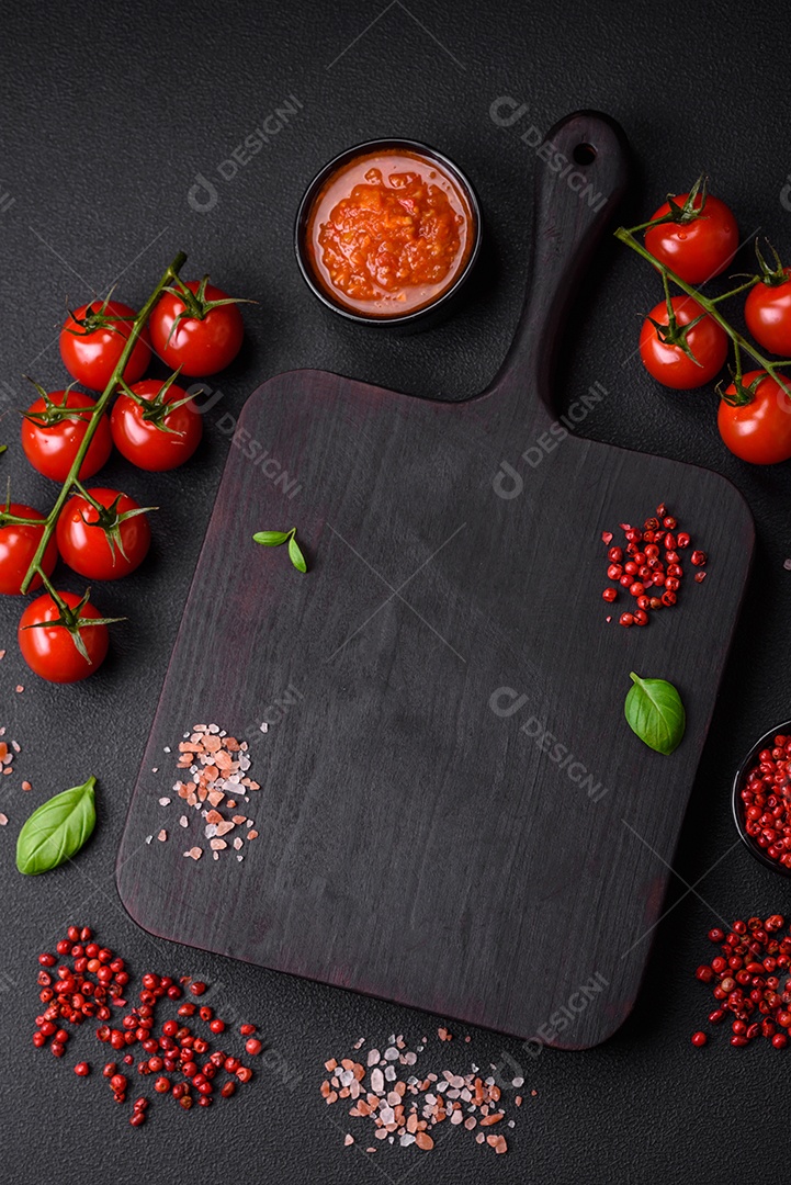 Massa de espaguete preta crua com tomate, sal, especiarias e ervas sobre um fundo escuro de concreto