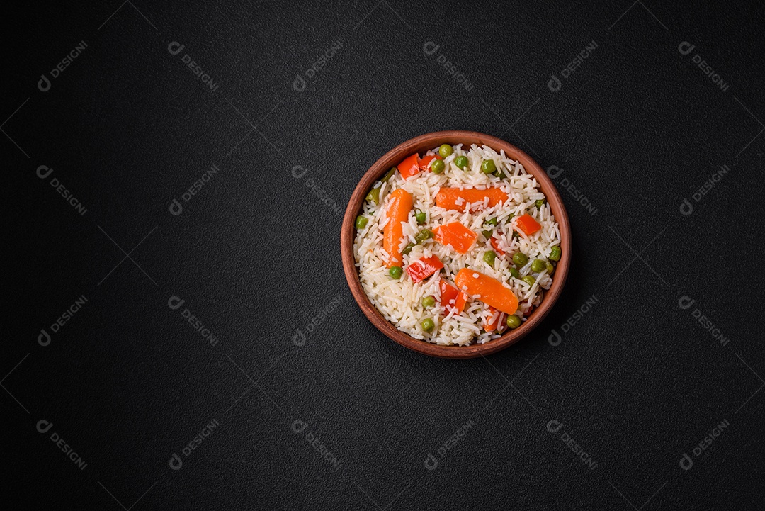 Delicioso arroz cozido com legumes ou risoto com sal, especiarias e ervas num prato cerâmico sobre fundo escuro de concreto