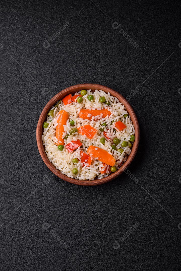 Delicioso arroz cozido com legumes ou risoto com sal, especiarias e ervas num prato cerâmico sobre fundo escuro de concreto