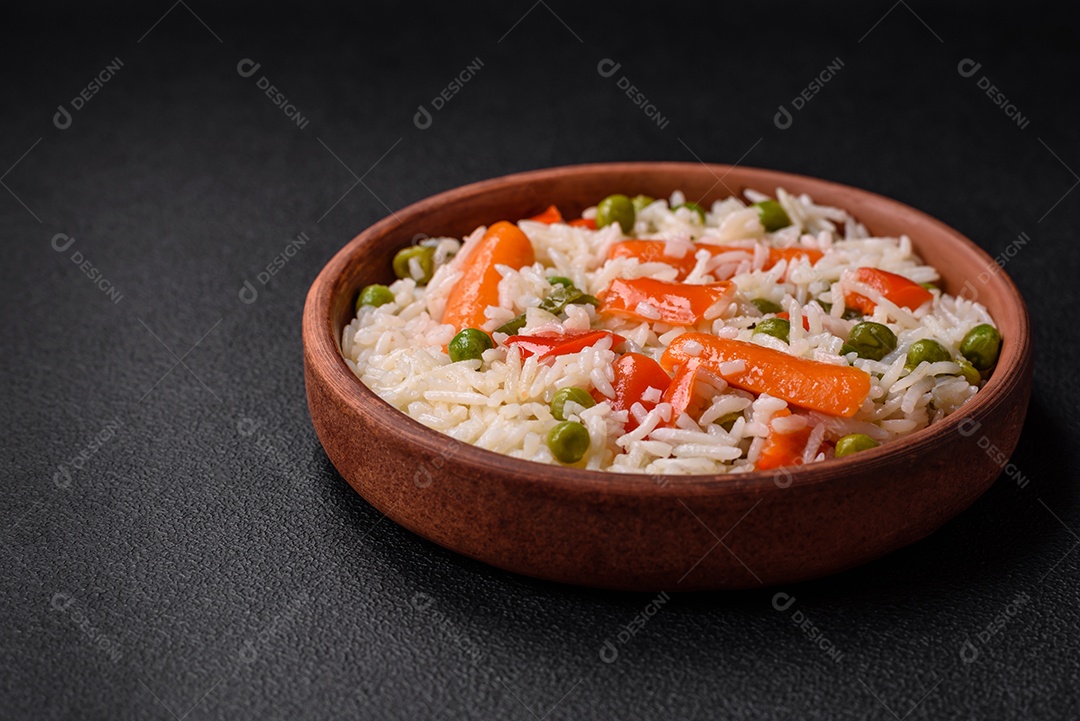 Delicioso arroz cozido com legumes ou risoto com sal, especiarias e ervas num prato cerâmico sobre fundo escuro de concreto