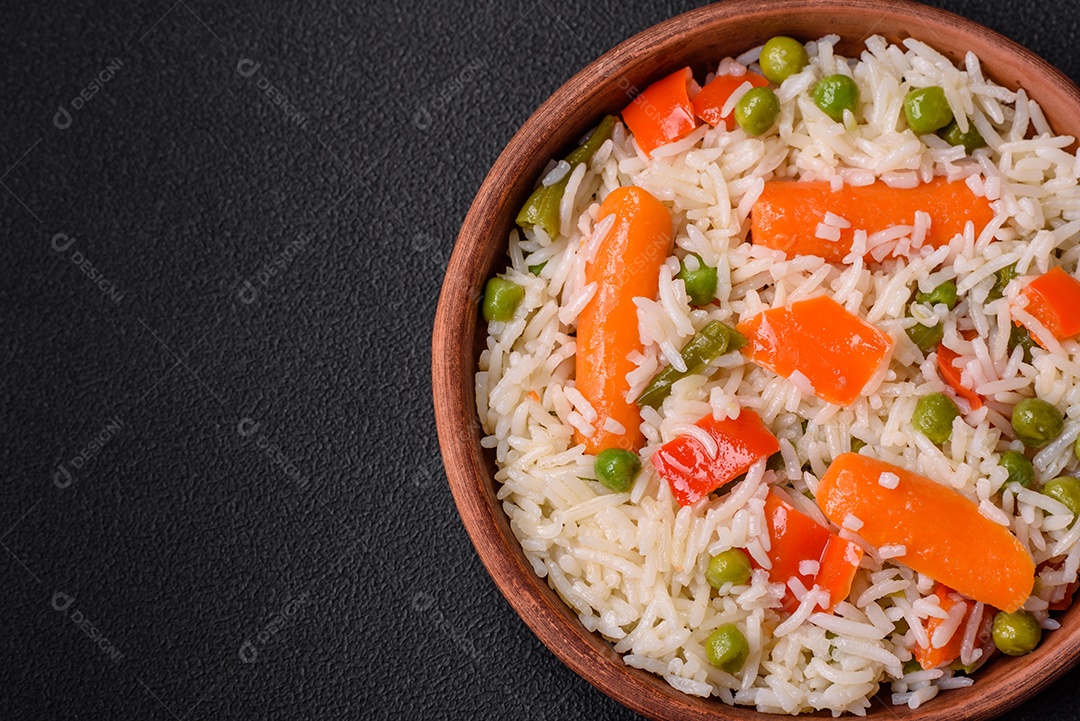 Delicioso arroz cozido com legumes ou risoto com sal, especiarias e ervas num prato cerâmico sobre fundo escuro de concreto