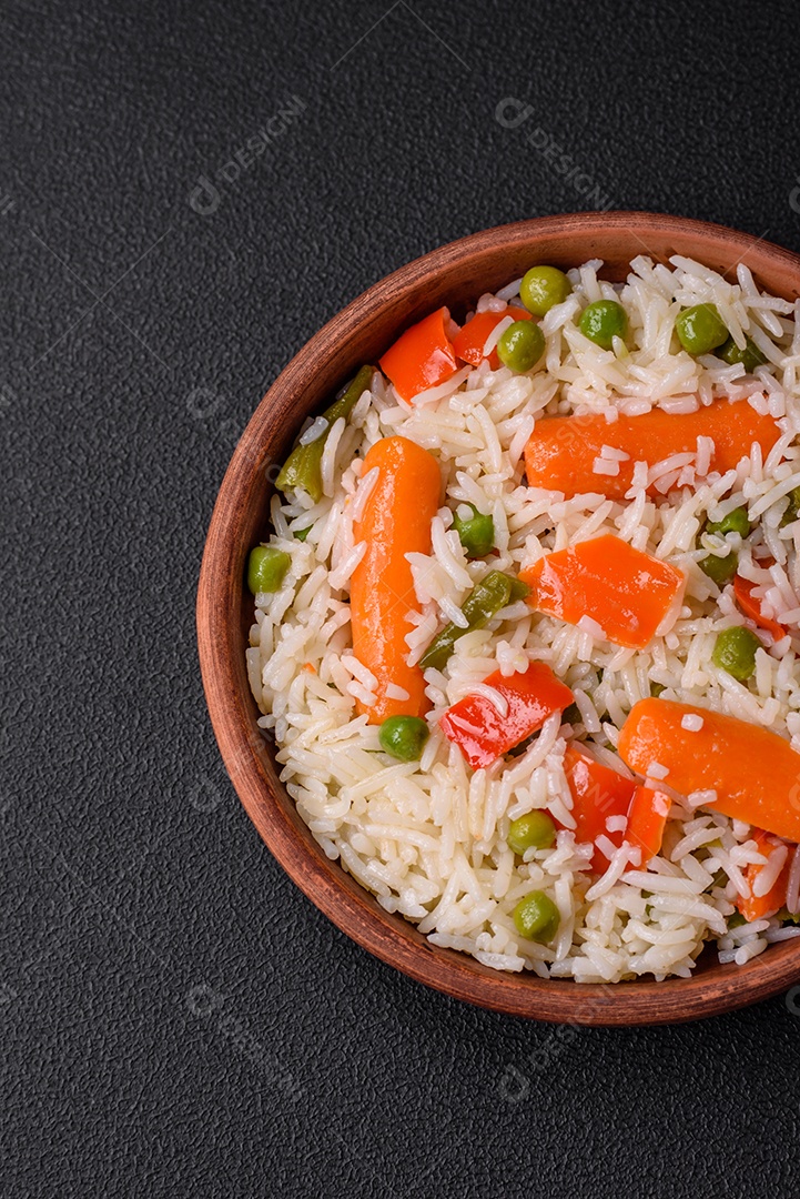 Delicioso arroz cozido com legumes ou risoto com sal, especiarias e ervas num prato cerâmico sobre fundo escuro de concreto