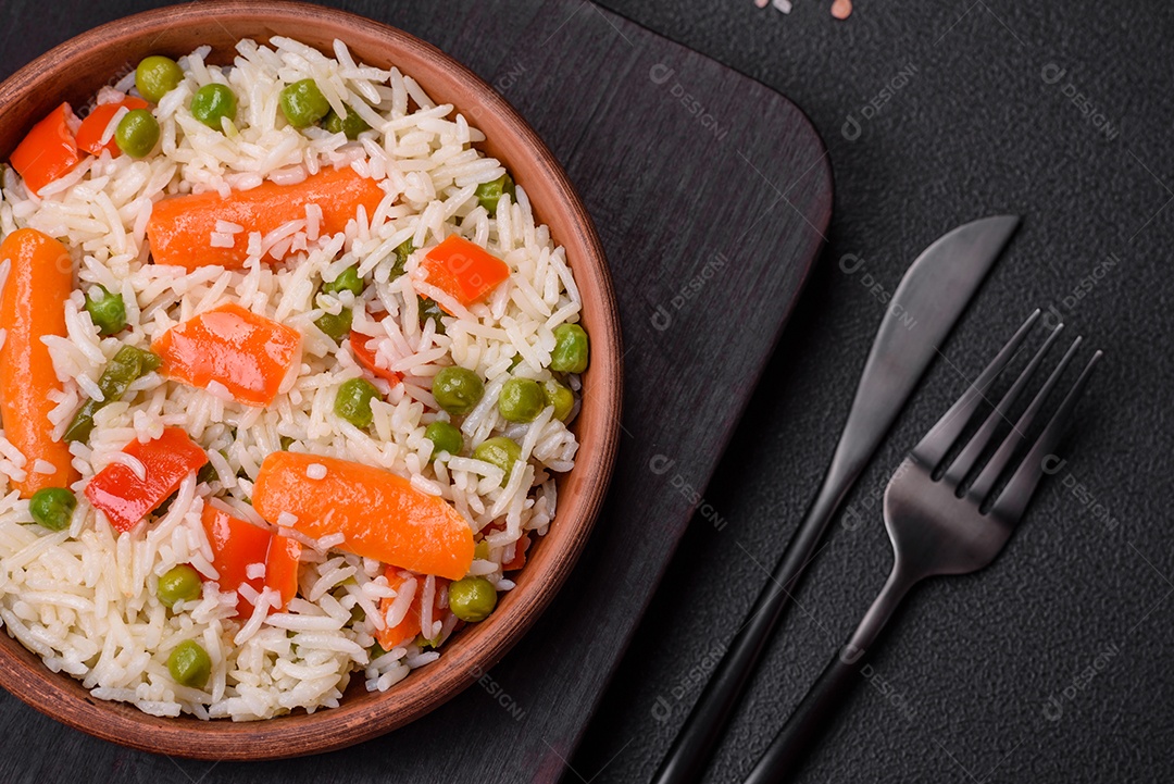 Delicioso arroz cozido com legumes ou risoto com sal, especiarias e ervas num prato cerâmico sobre fundo escuro de concreto