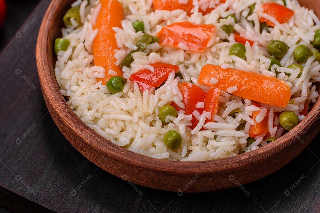 Delicioso arroz cozido com legumes ou risoto com sal, especiarias e ervas num prato cerâmico sobre fundo escuro de concreto