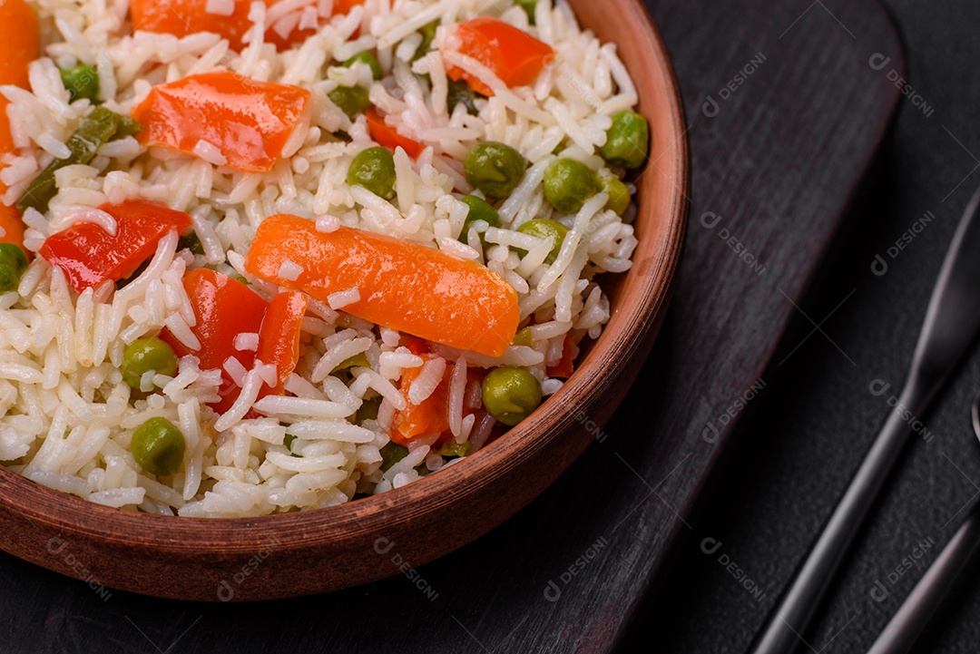 Delicioso arroz cozido com legumes ou risoto com sal, especiarias e ervas num prato cerâmico sobre fundo escuro de concreto