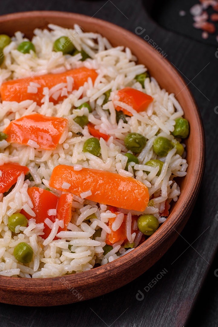 Delicioso arroz cozido com legumes ou risoto com sal, especiarias e ervas num prato cerâmico sobre fundo escuro de concreto
