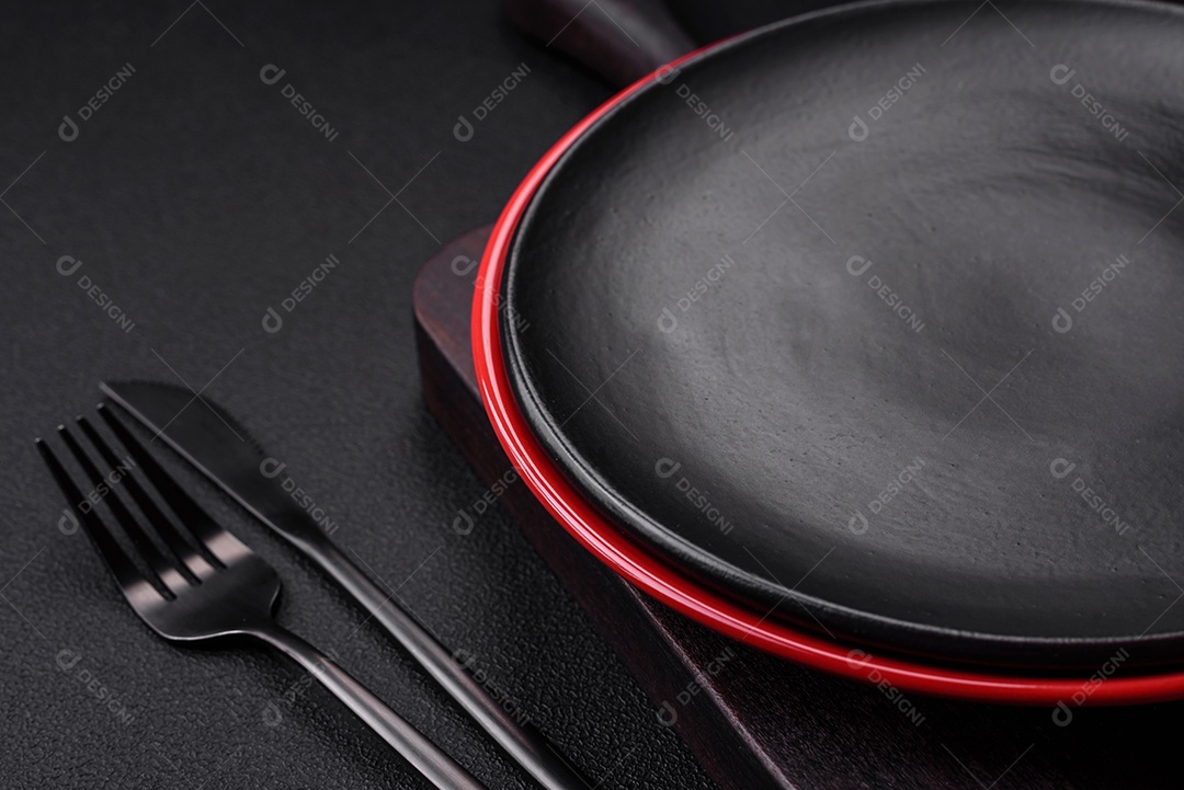 Placa cerâmica vazia em fundo de concreto texturizado escuro. Talheres na mesa da cozinha