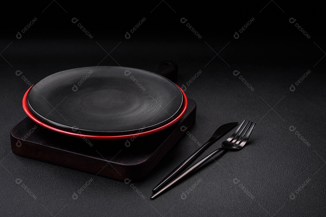 Placa cerâmica vazia em fundo de concreto texturizado escuro. Talheres na mesa da cozinha